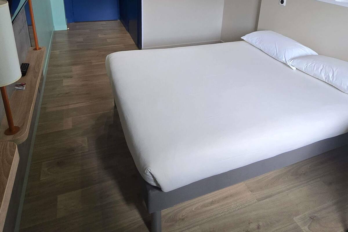 A neatly made bed with a wooden floor and a blue wall in the background.