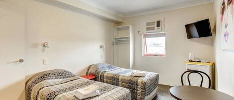 Una habitación con dos camas, una mesita, una silla, un televisor montado en la pared y una ventana con vistas.