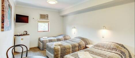 A small, well-lit room with two single beds, a desk with a chair, and a small table.
