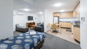 Una habitación pequeña con cama, escritorio, sofá y kitchenette.