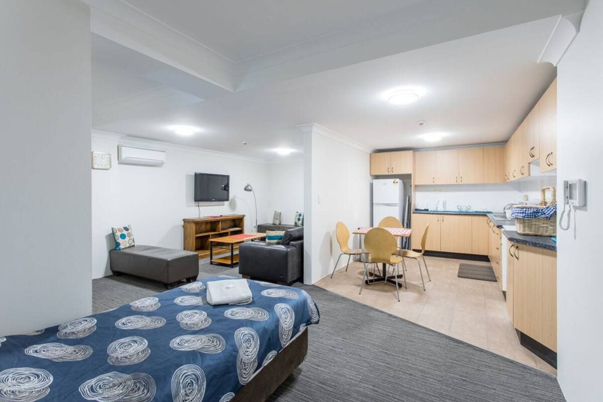 A compact room with a bed, a desk, a sofa, and a kitchenette.