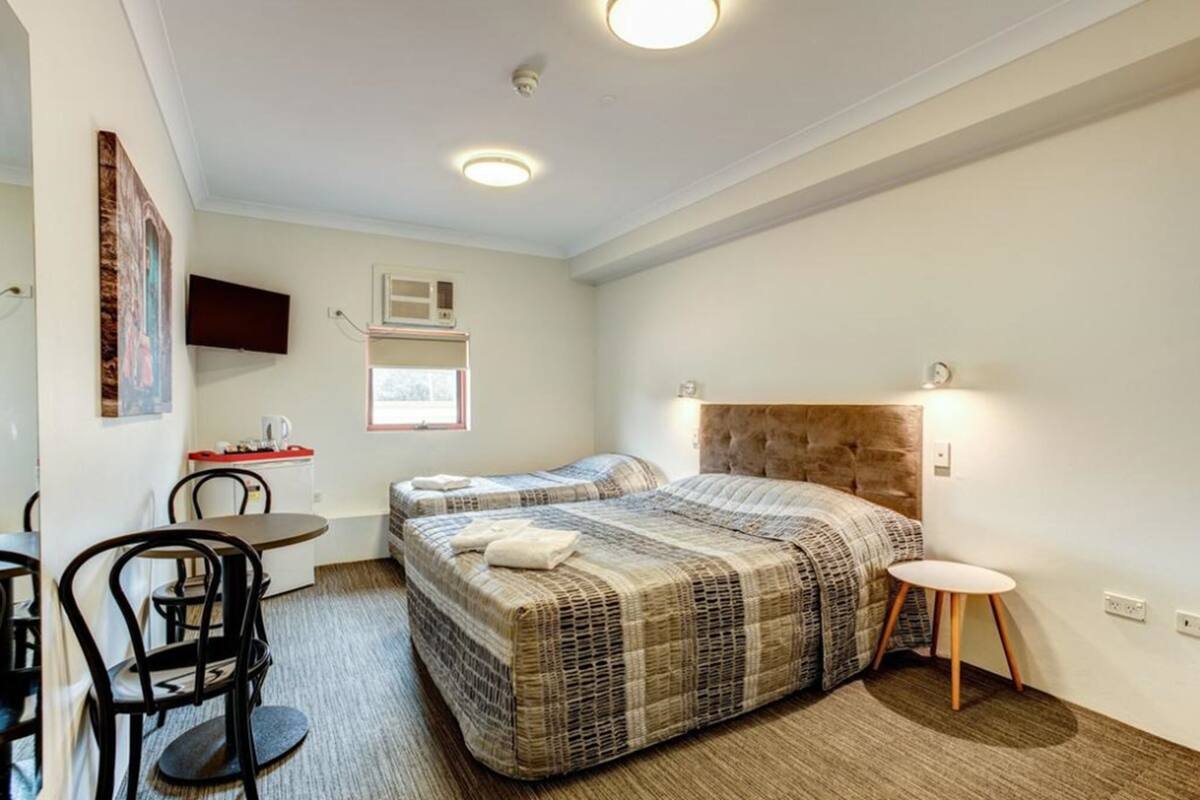 A hotel room with two beds, a desk, chairs, a TV, and a window.