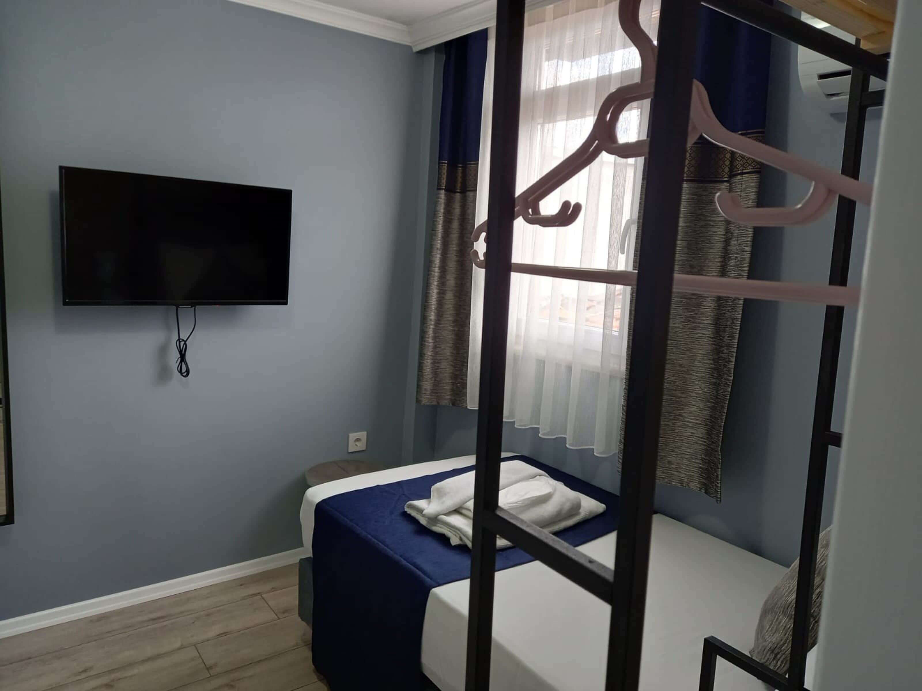 A bedroom with a bunk bed, a flat-screen TV mounted on the wall, and a window with curtains.