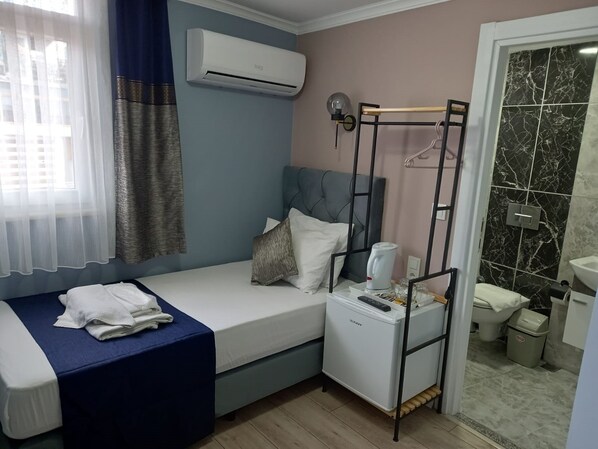 A compact hotel room with a single bed, a small bedside table with a lamp, an air conditioner, and a view of the bathroom.