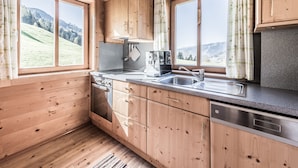 A wooden cabin kitchen with wooden cabinets, a stove, a sink, and a dishwasher. - Ferienhof Oberreit (Bruck an der Grossglocknerstrasse)