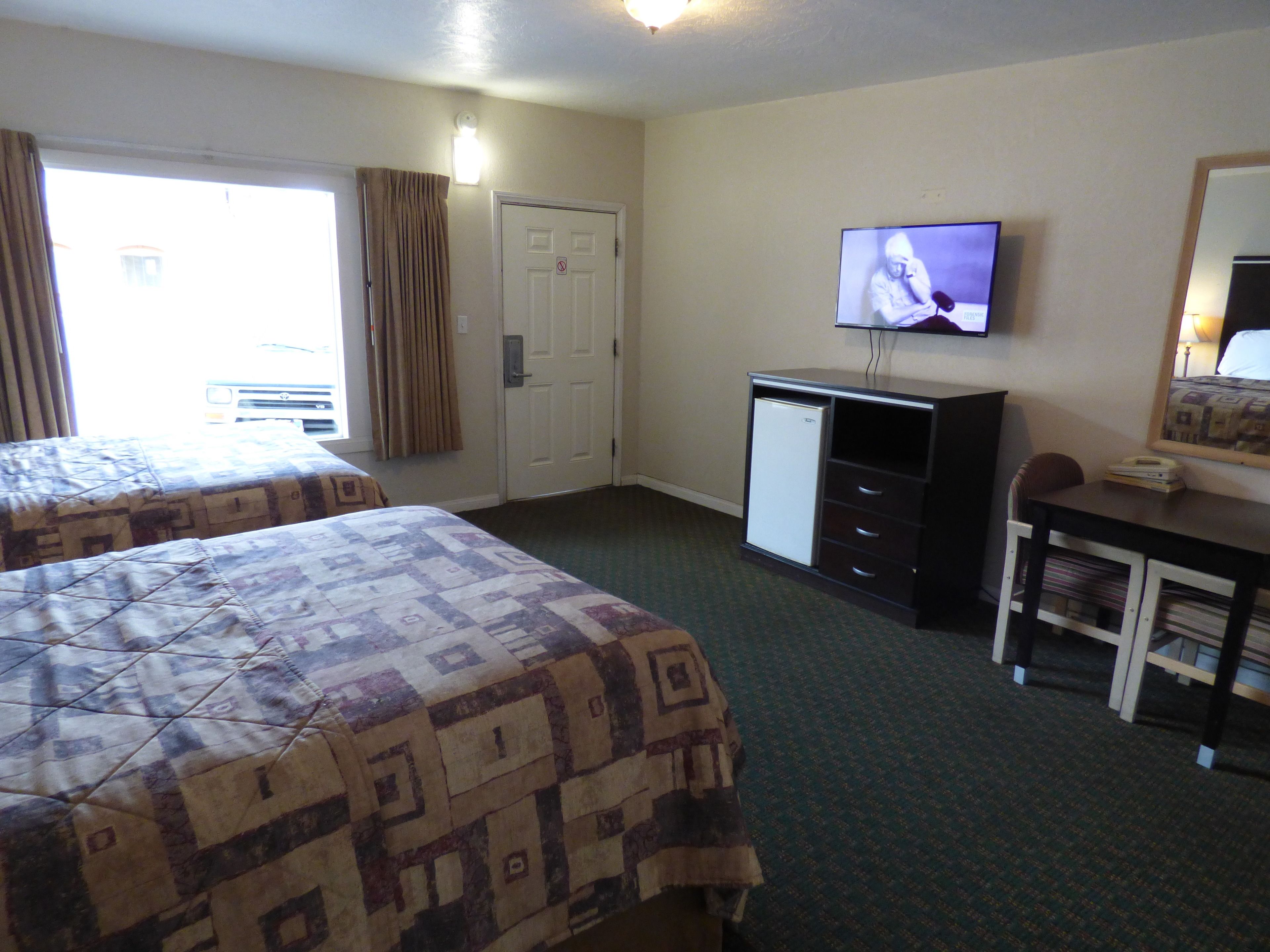A hotel room with two beds, a desk, a television, and a door.