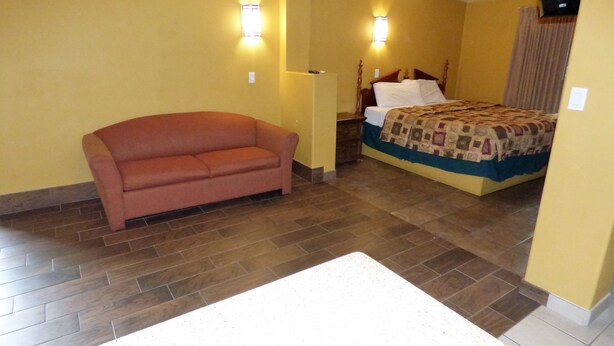 A hotel room with a sofa, a bed with a quilt, and a nightstand. - Sands Motel (St. George)