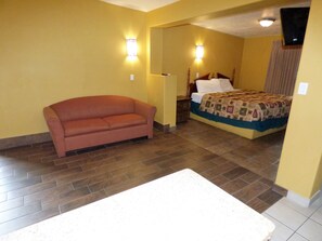 Una camera d'albergo con un divano, un letto con copripiumino e un comodino.
