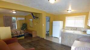 A compact living space with a kitchenette, a dining area, and a bedroom with a bed and a bench. - Sands Motel (St. George)