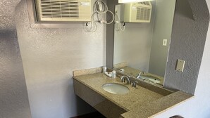 A bathroom with a granite countertop sink, a mirror, and a wall-mounted air conditioning unit. - Sands Motel (St. George)