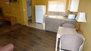 A compact kitchen with a refrigerator, a sink, and a dining area with chairs. - Sands Motel (St. George)