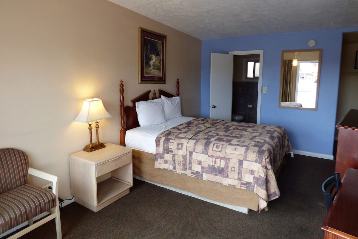 Quarto de hotel com uma cama, mesa de cabeceira com abajur, uma cadeira e cômoda.