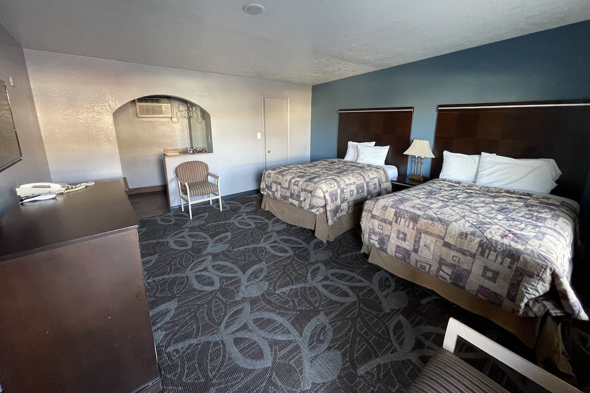 Quarto de hotel com duas camas, uma mesa, uma cadeira e uma pequena cozinha.