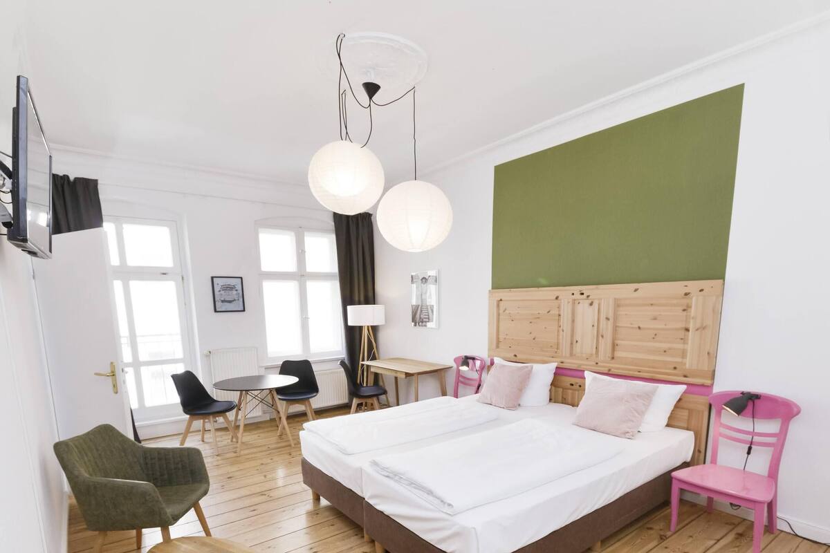 Een moderne hotelkamer met een groot bed, houten vloer, een groene accentmuur en een zithoek met stoelen en een tafel.