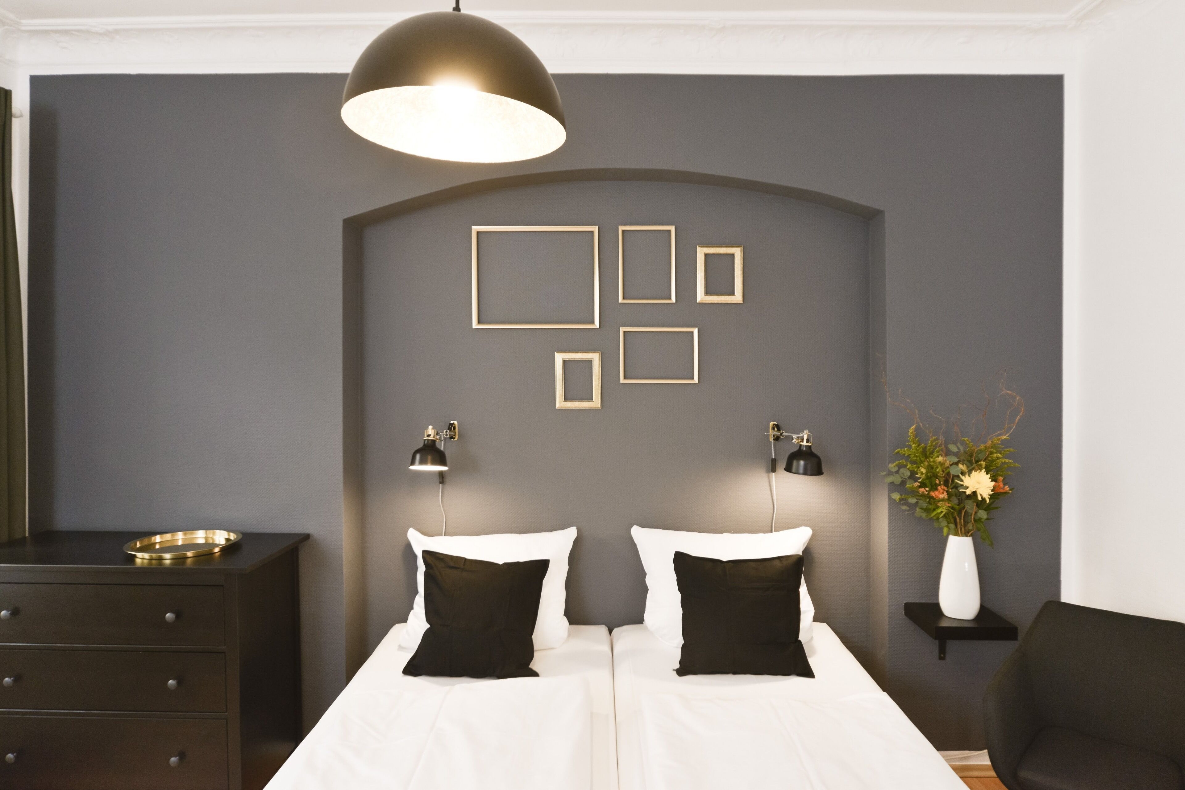 A bedroom with a double bed, two bedside tables, a dresser, a pendant light, and a wall-mounted picture frame.