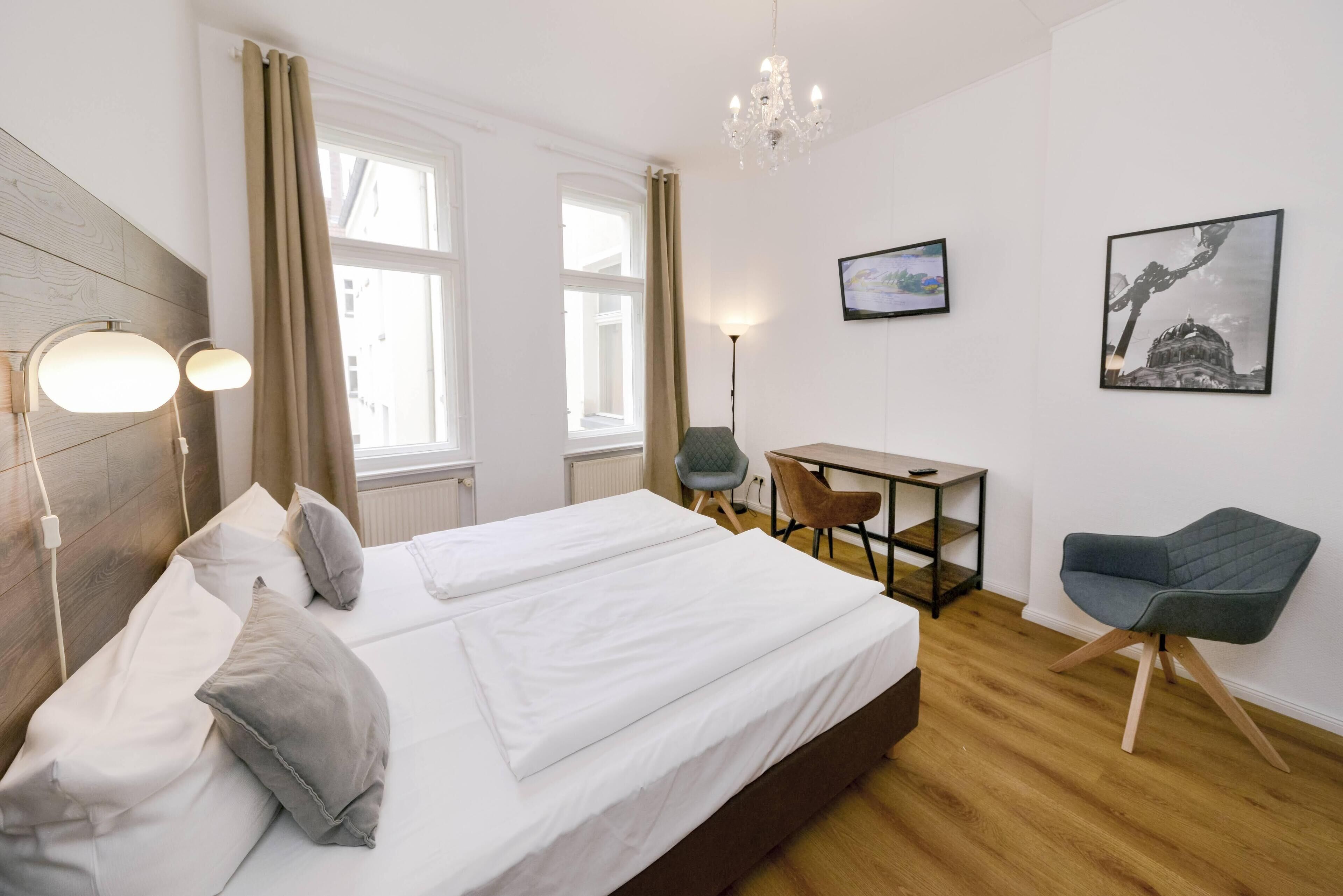 Ein Hotelzimmer mit einem großen Bett, einem Schreibtisch, zwei Stühlen, einer Chandelierleuchtre und Kunstwerken an den Wänden.