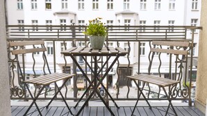 A balcony with a wooden table and two benches, a potted plant, and a view of buildings in the background.