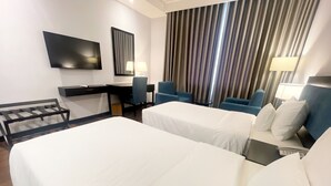 Une chambre d’hôtel avec deux lits, un bureau, une chaise, une télévision et une grande fenêtre avec des rideaux.