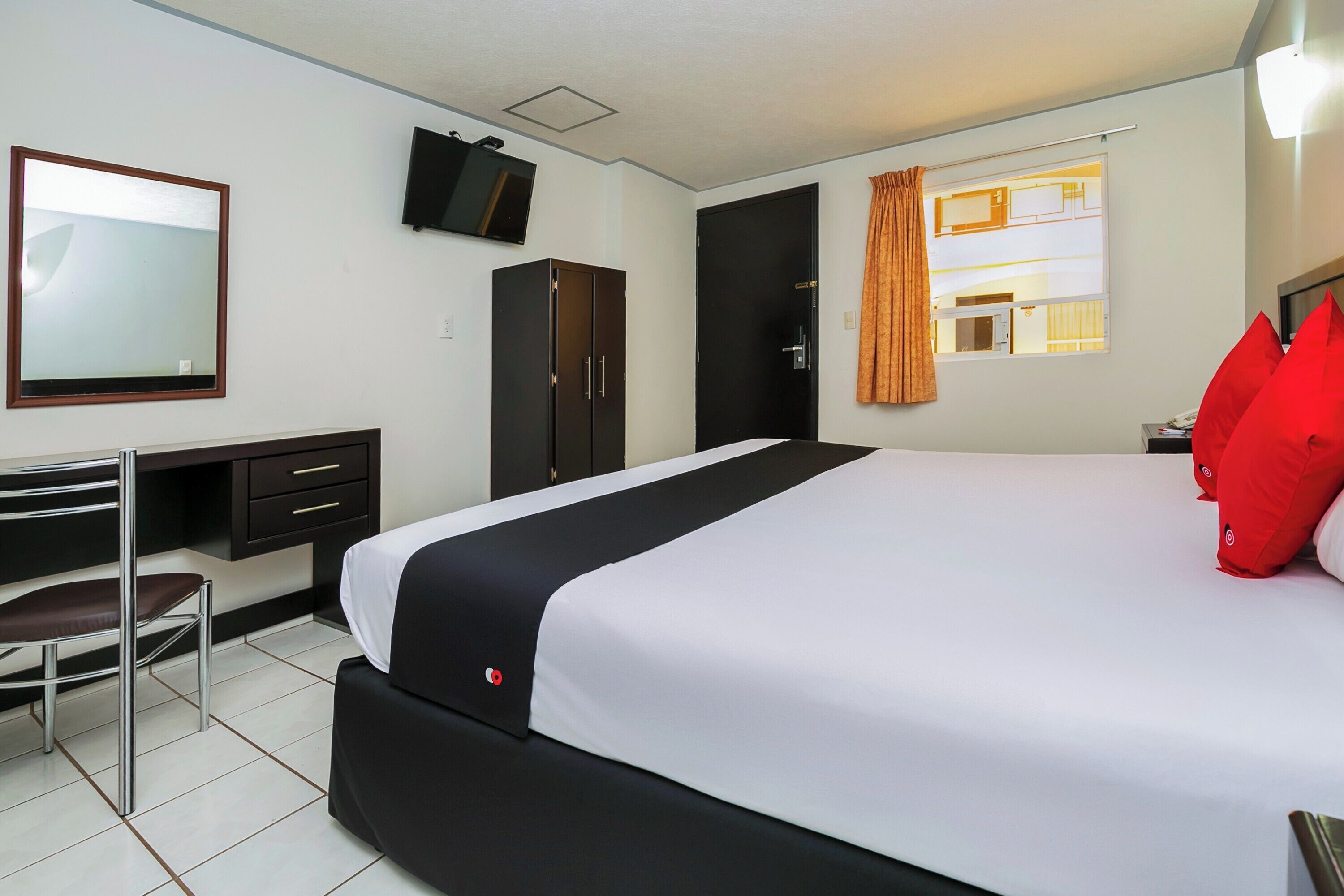 Ein Hotelzimmer mit Bett, Schreibtisch mit Stuhl, Kleiderschrank, Wandfernseher und einem Fenster mit Vorhängen.