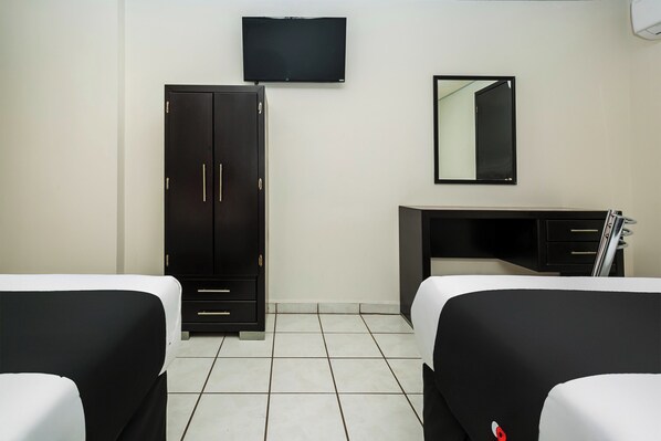 A hotel room with two beds, a wardrobe, a desk, a television, and a mirror.