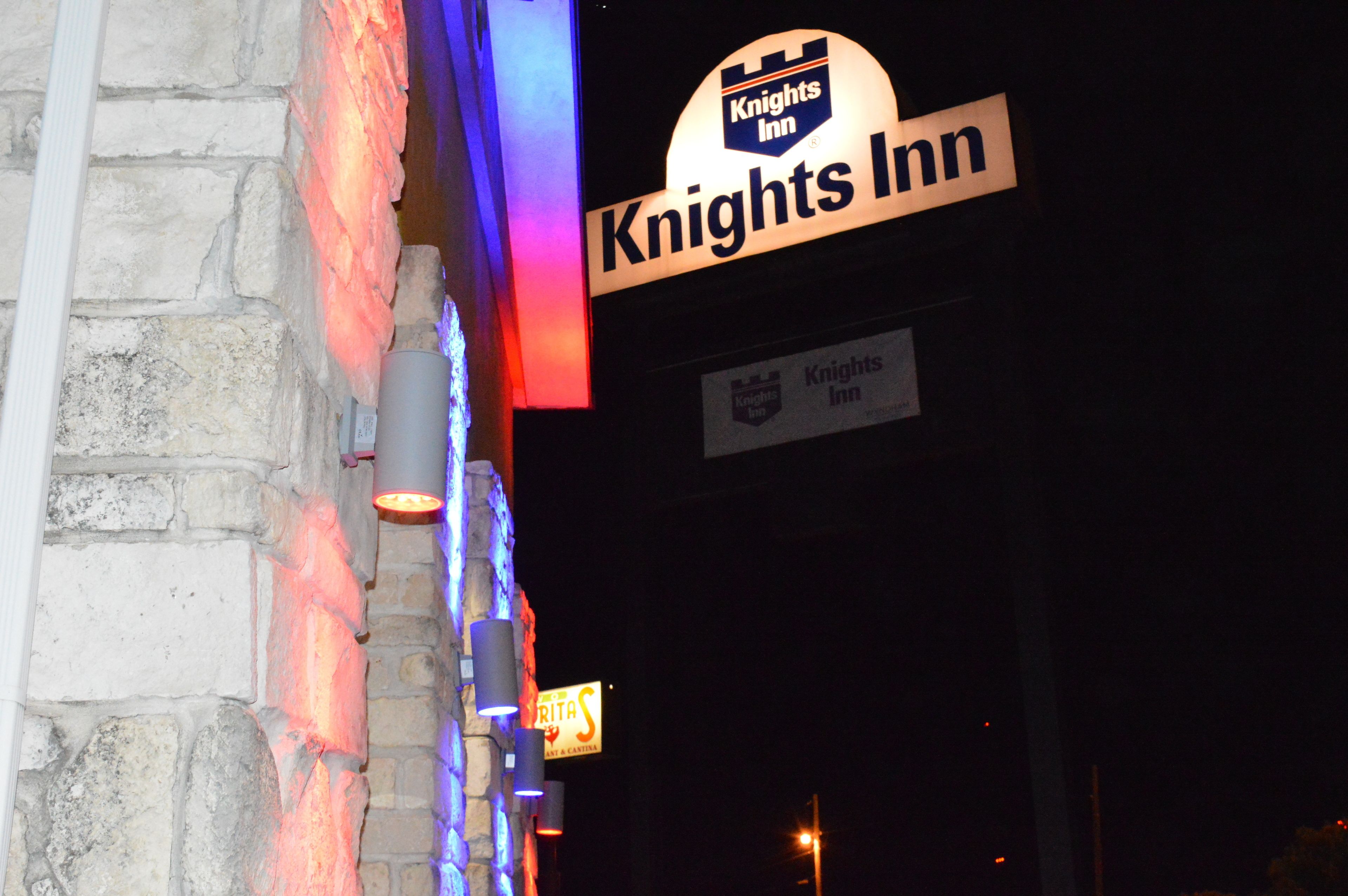 A Knights Inn sign with a stone wall backdrop and a neon sign.
