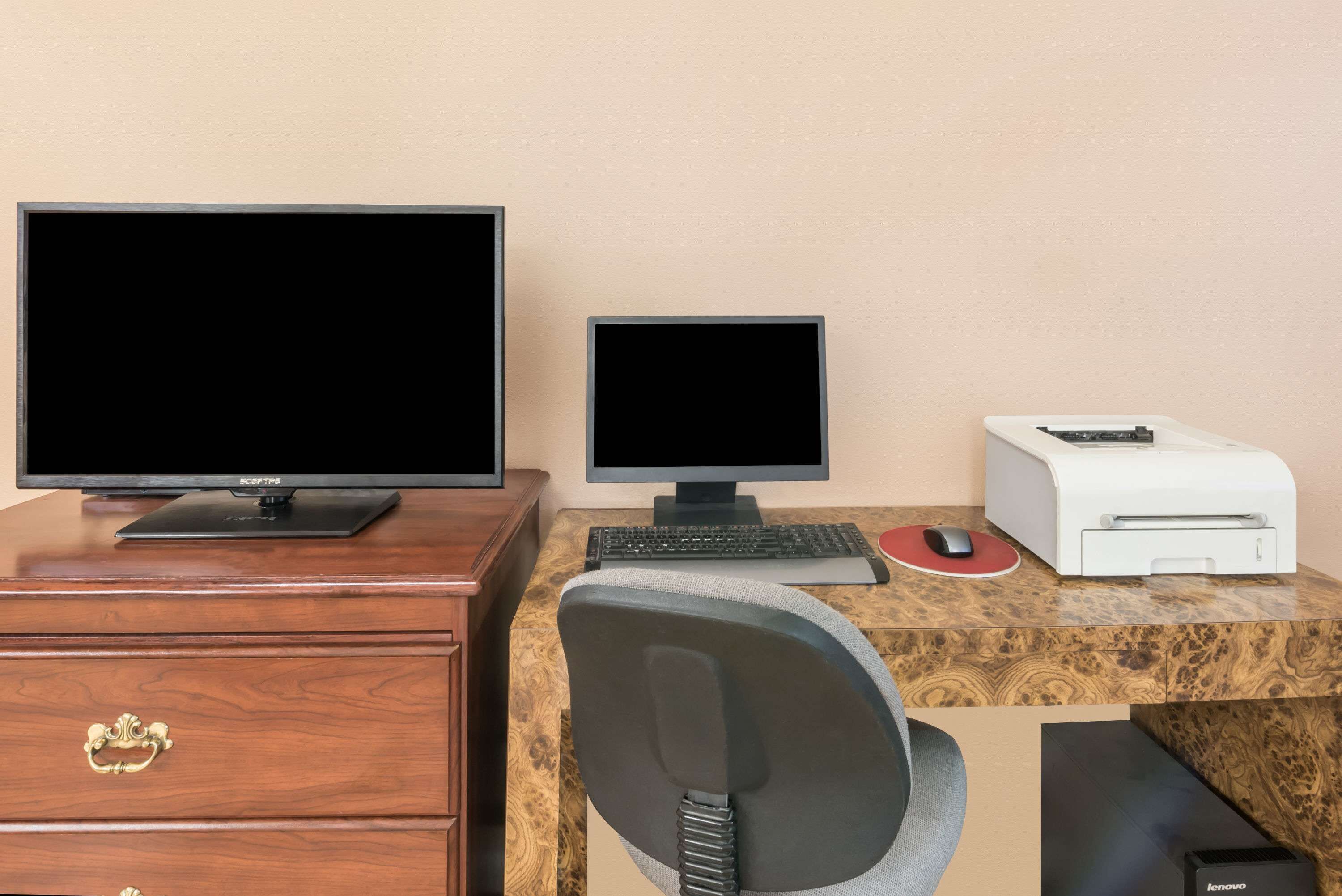 A wooden desk with two monitors, a keyboard, a mouse, a printer, and a chair.