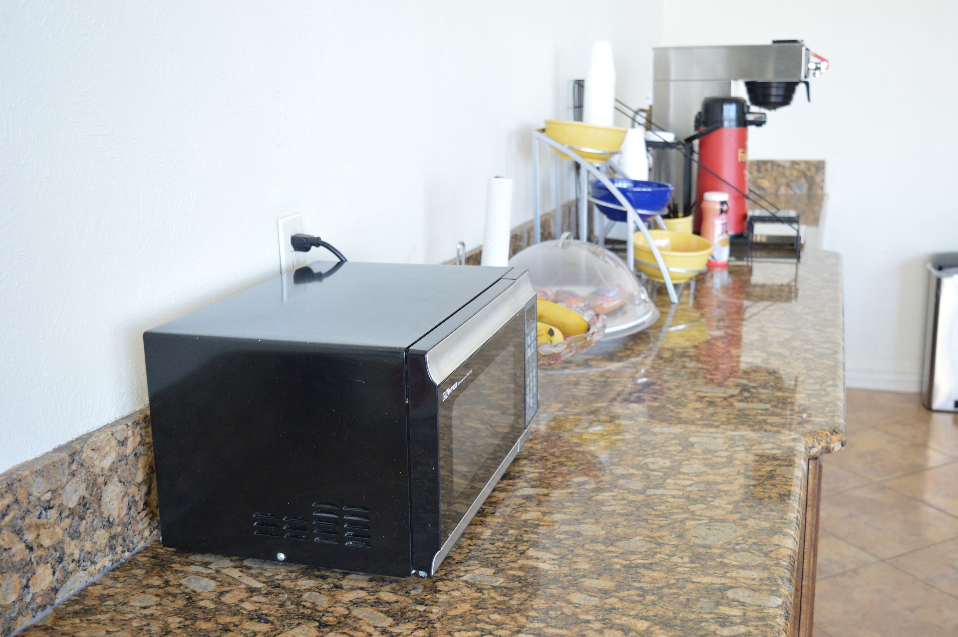 A kitchen with a microwave on the counter, a coffee maker, and a trash can.