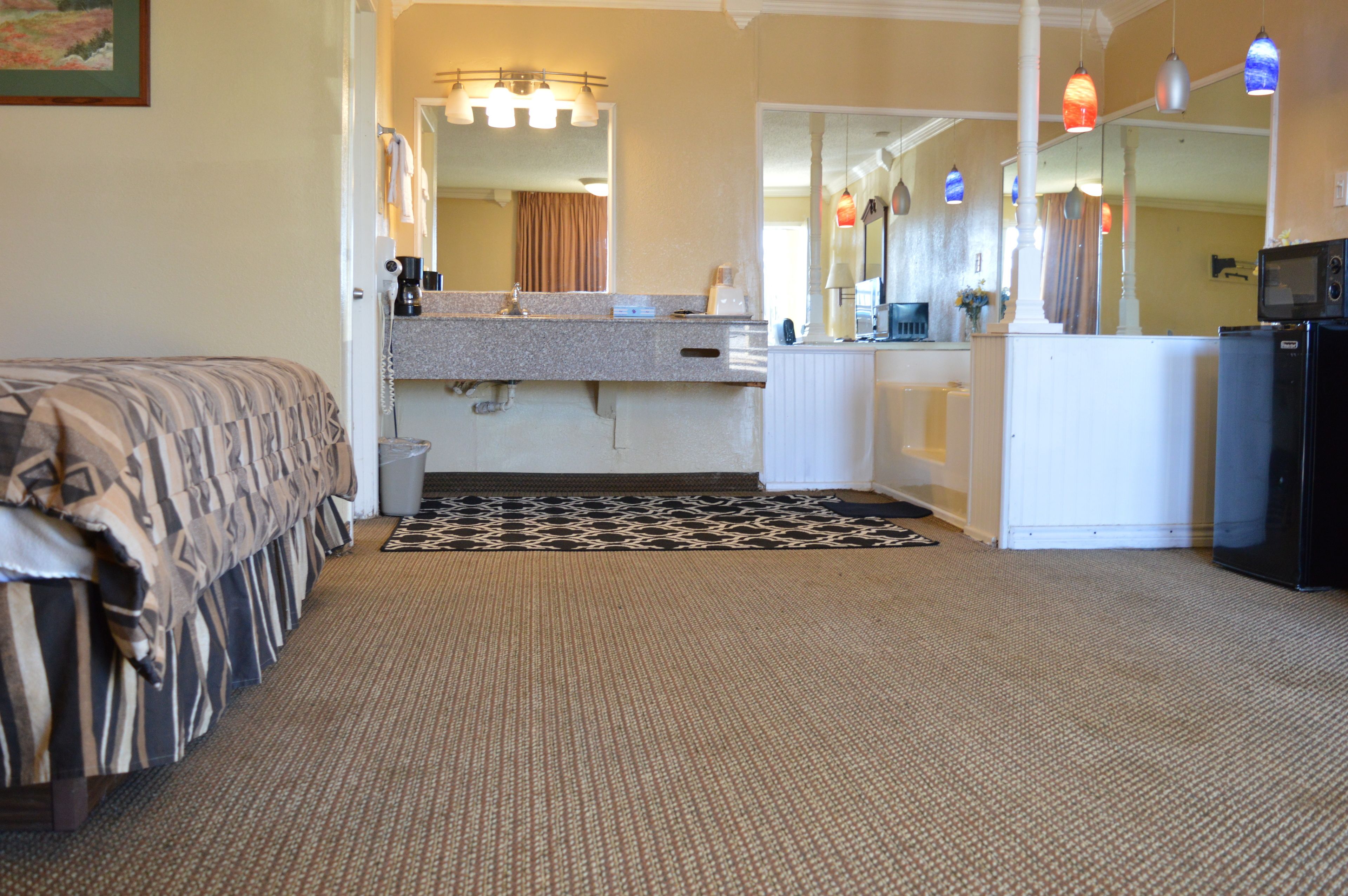 Habitación de hotel con cama, baño con lavamanos y espejo, y un refrigerador.