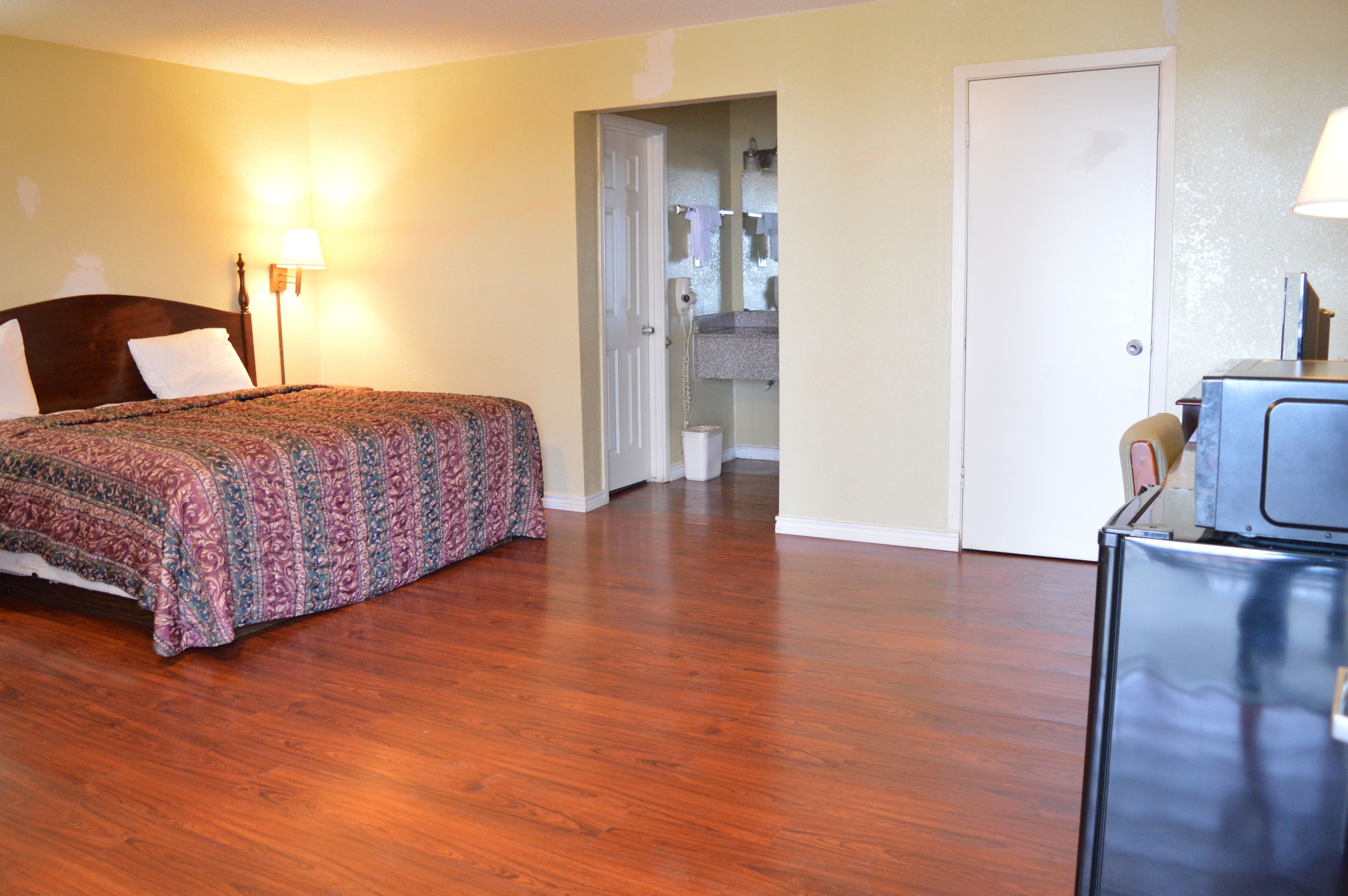Une chambre d’hôtel avec un plancher en bois, un lit recouvert d’une courtepointe à motifs, un bureau avec une lampe et une porte donnant sur une salle de bain.