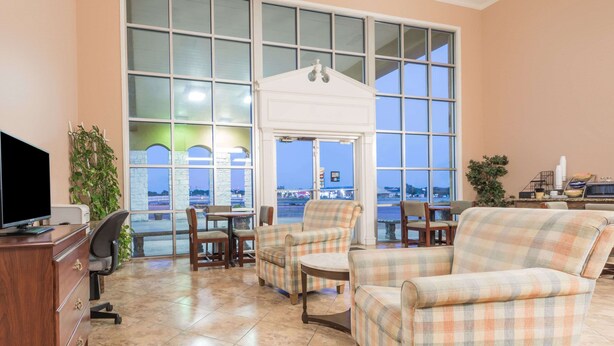 A hotel room with large windows, a television, a desk, and a chair. - Knights Inn Greenville, TX (Greenville)