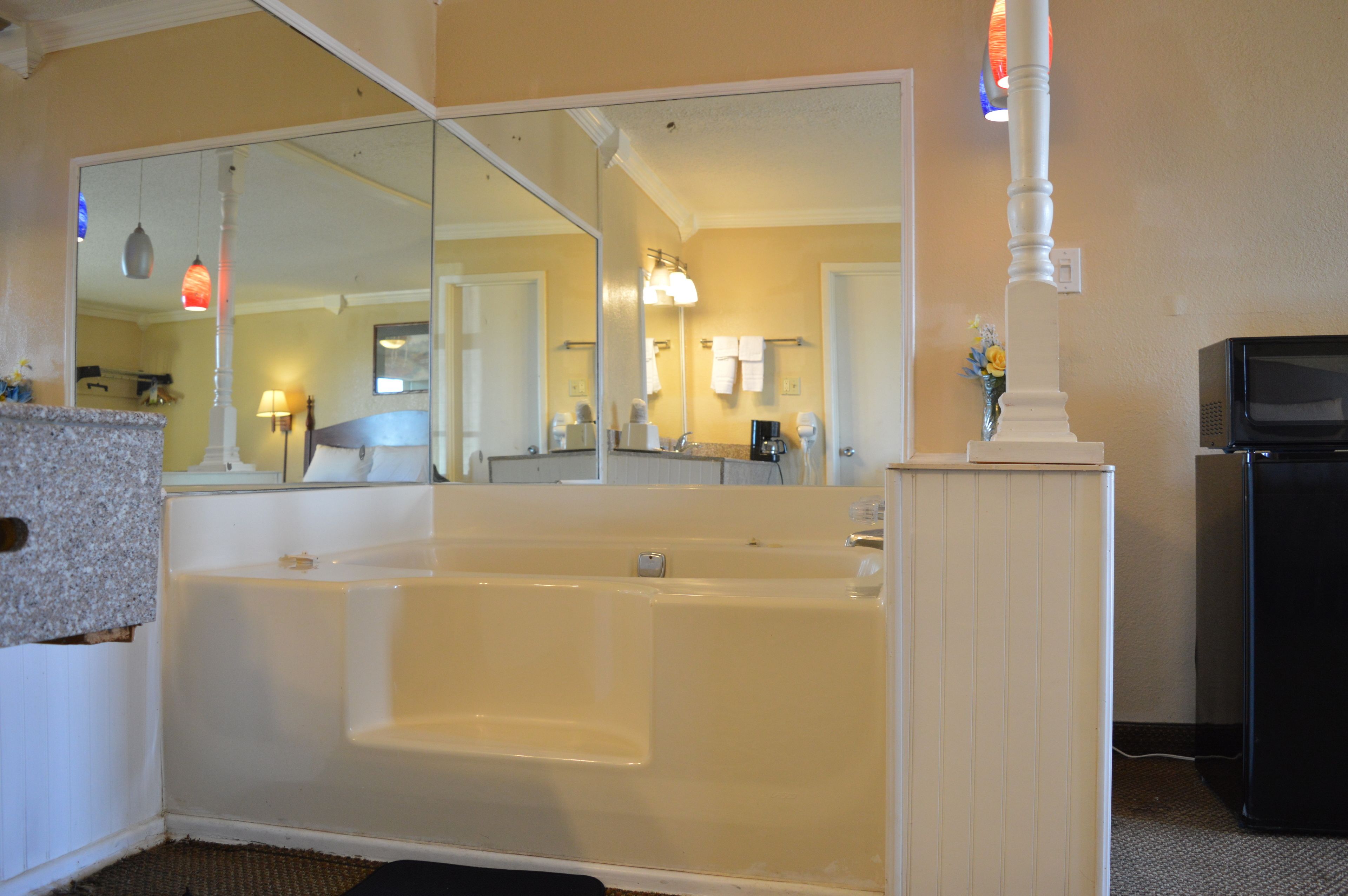 A bathroom with a large bathtub, a mirror, a sink, and a television.