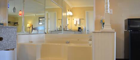 A bathroom with a large bathtub, a mirror, a sink, and a television.