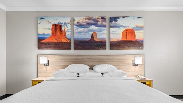 A hotel room with a large bed, a wooden headboard, and three paintings of rock formations on the wall.