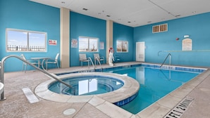An indoor swimming pool with a hot tub, lounge chairs, and safety signs.