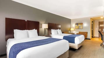A hotel room with two beds, a wooden headboard, a lamp, and a painting on the wall.