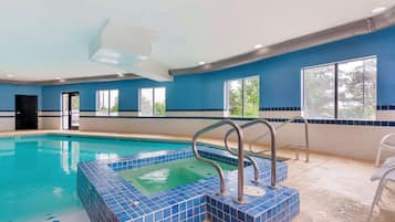 Une piscine intérieure avec des marches et des rampes recouvertes de carreaux bleus, de grandes fenêtres et une porte.