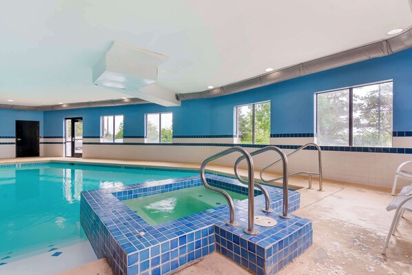 An indoor swimming pool with blue-tiled steps and handrails, large windows, and a door.