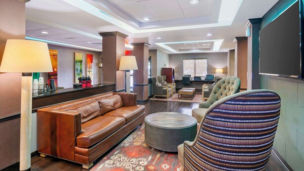 A modern hotel lobby with a leather sofa, a patterned armchair, and a flat-screen TV on the wall. - Best Western Plus Olathe Hotel (Olathe)