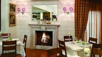 A dining area with a fireplace, wooden chairs, and tables set for a meal.