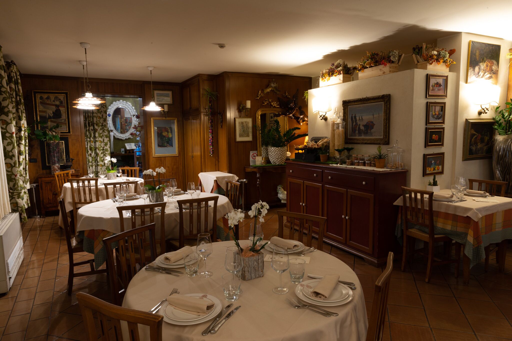 Uma área de refeições com mesas redondas para quatro pessoas, cadeiras de madeira e um balcão de buffet com diversos pratos.