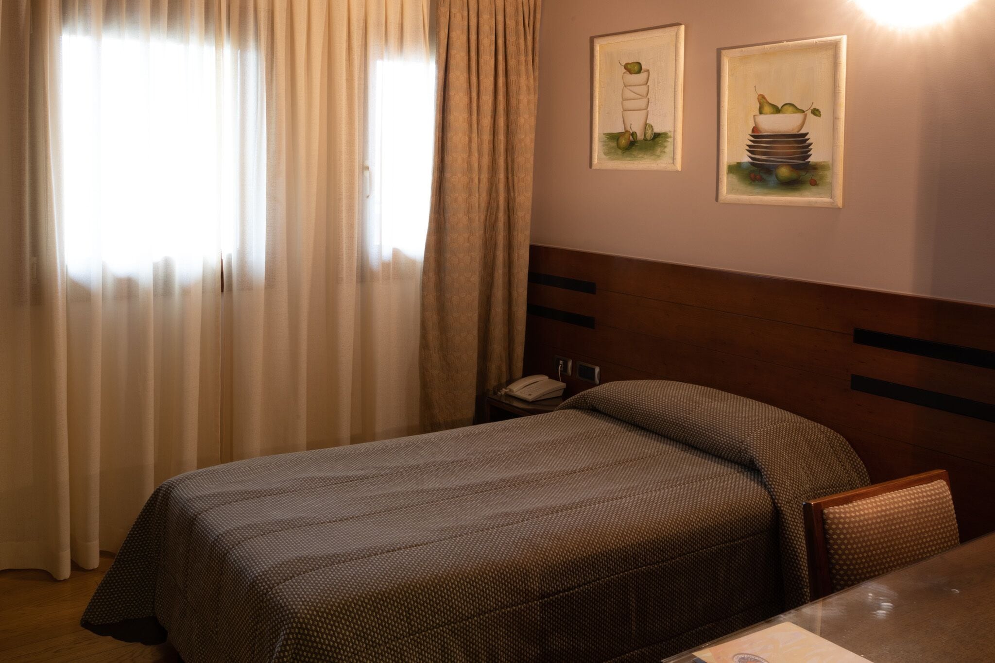 Een hotelkamer met een bed, een stoel, een tafel en twee kunstwerken in lijsten aan de muur.