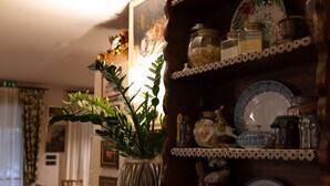 A cozy room with a wooden shelf holding various kitchen items like jars and plates, a vase with green leaves, and a framed picture on the wall. - Locanda Al Sole (Castello di Godego)