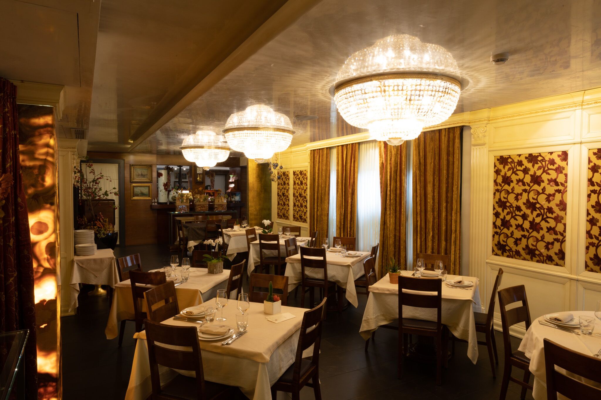 Ein Restaurant mit mehreren Tischen, jeder Tisch ist mit einer weißen Tischdecke und Stühlen gedeckt.