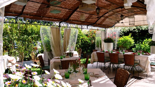 An outdoor dining area with tables set for meals, surrounded by lush greenery and flowers. - Locanda Al Sole (Castello di Godego)