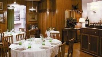 Un comedor con mesas redondas dispuestas para cuatro personas, paneles de madera en las paredes y un aparador con una botella de vino y una lámpara.