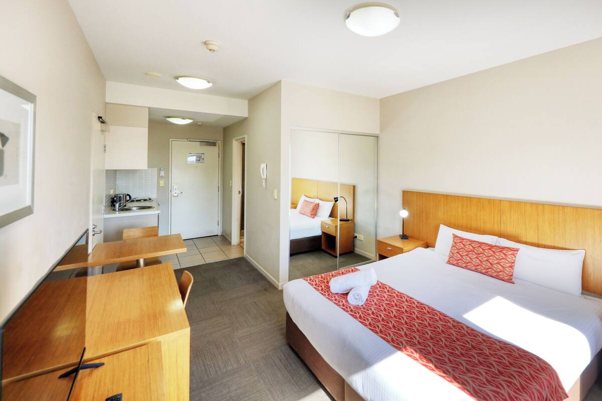 A hotel room with a large bed, bedside tables, a desk, and a kitchenette.