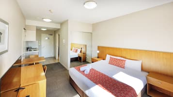 Una habitación de hotel con una cama grande, mesitas de noche, un escritorio y una kitchenette.