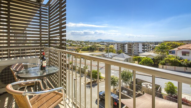 Un balcón con mesa y sillas, con vista a un paisaje urbano de edificios y áreas verdes.