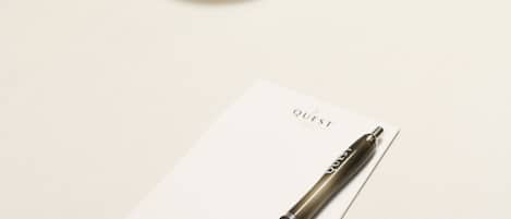 A conference table with a white tablecloth, a white cup and saucer, a bowl of snacks, and a pen on a piece of paper labeled "QUEST".