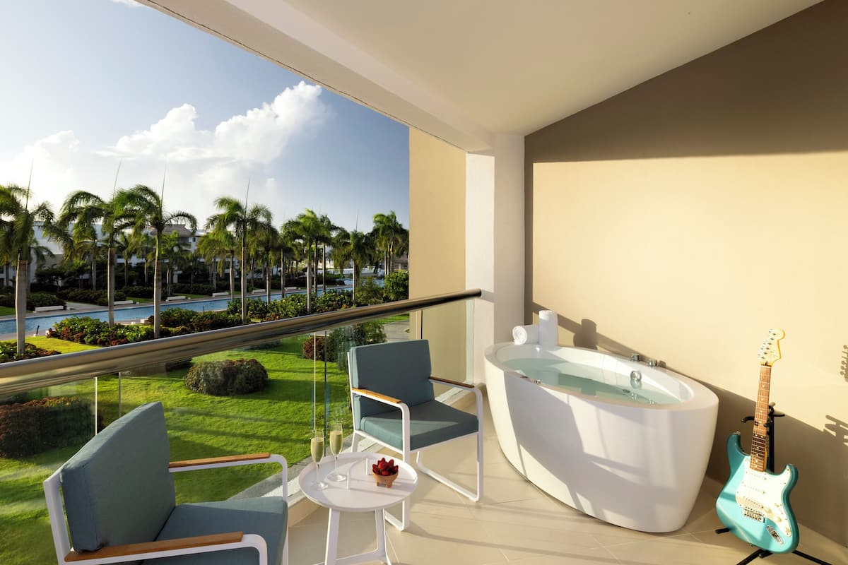 Ein Balkon mit Blick auf einen Pool und Palmen, einem Whirlpool, einer Gitarre und zwei Stühlen.